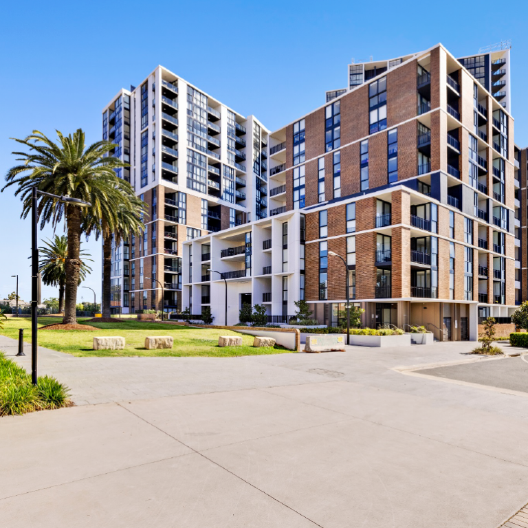 Nine story L shaped building with large lawn and gardens outside and a palm tree