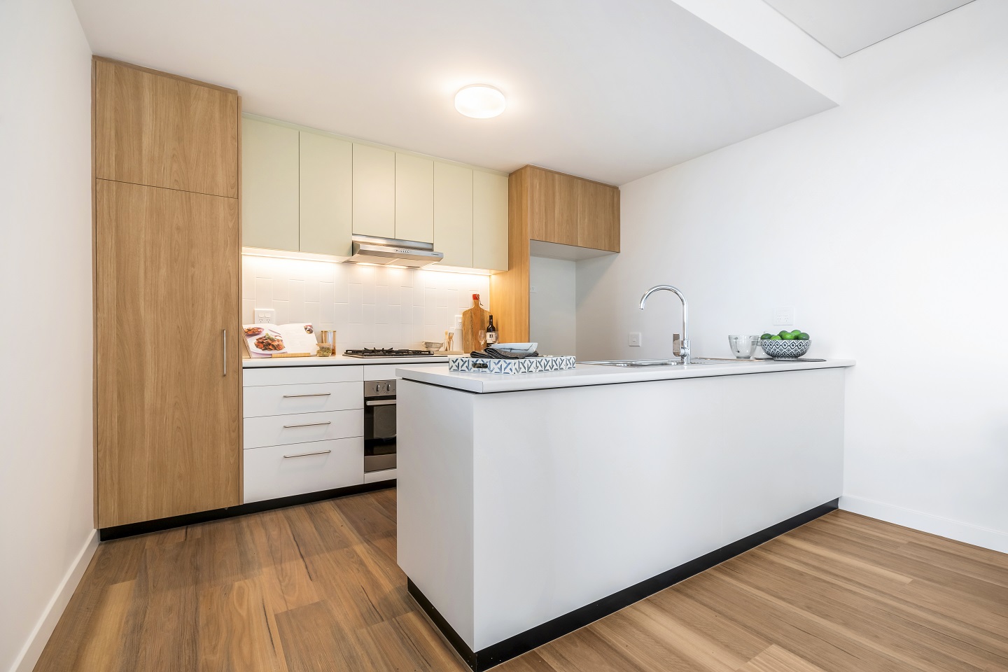 Kitchen area of bright, clean unit, showing rangehood, oven, sink, kitchen bench