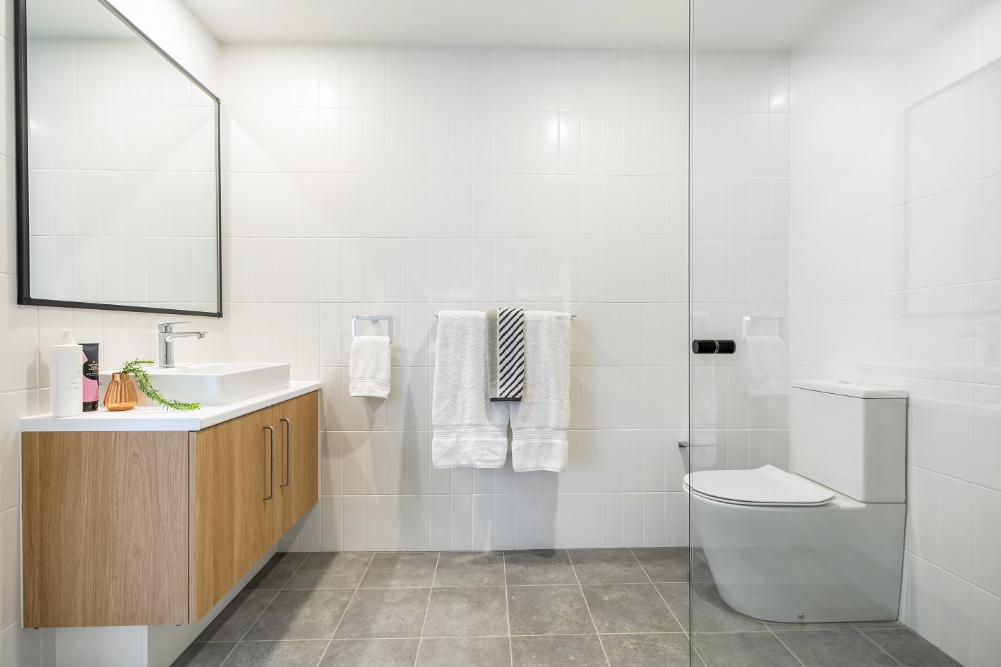 Spacious bathroom area of bright, clean unit. Grey tiling and large mirror.