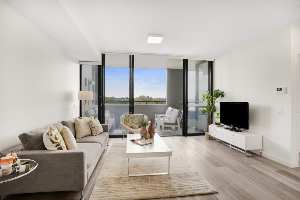 Lounge area of display furnished unit looking through to balcony and view over the suburbs