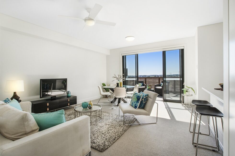 Lounge area of display furnished unit looking through to balcony and view over the suburbs