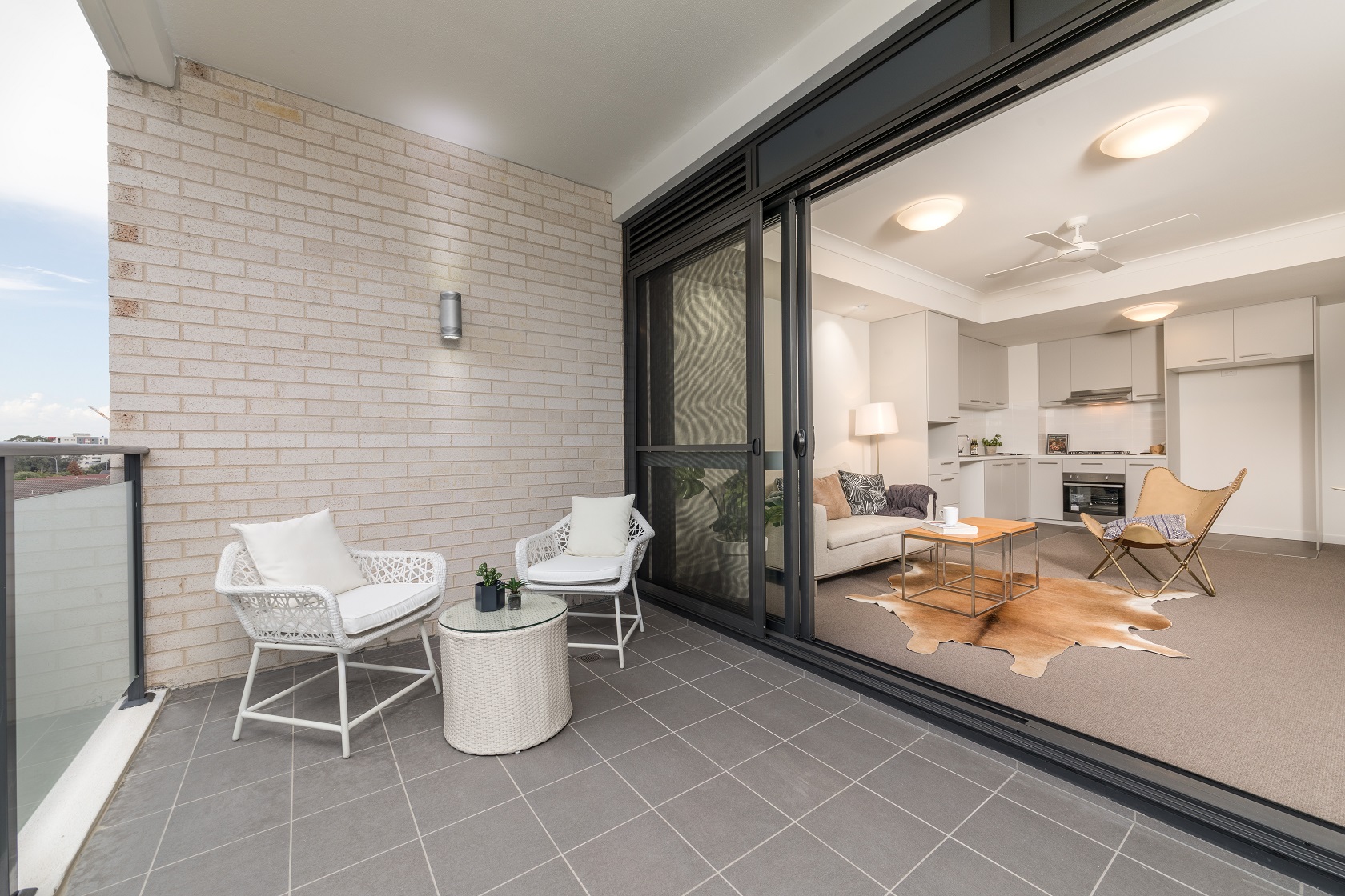 View into a display furnished unit from the balcony, with large sliding and screen doors open