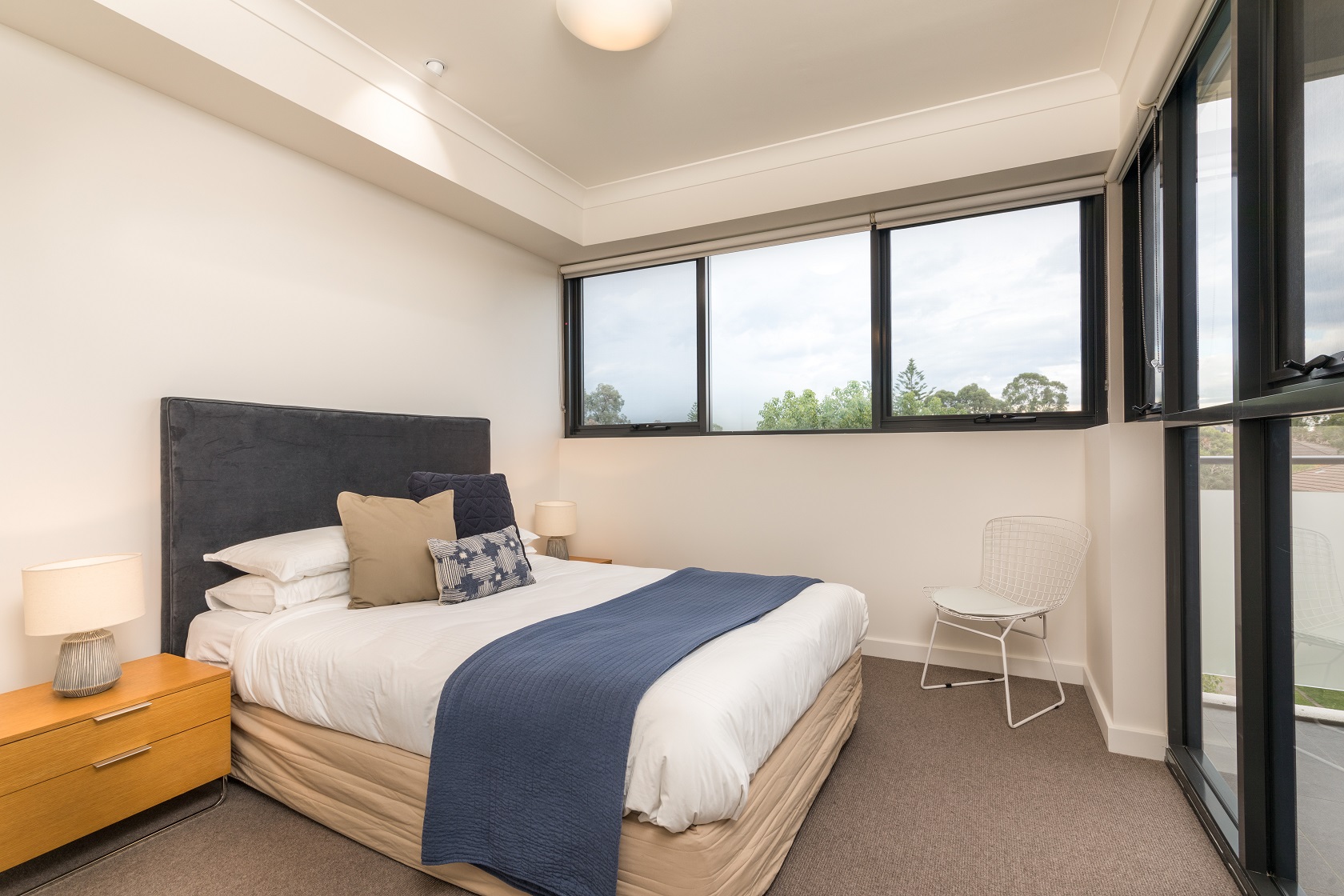 Main bedroom of display furnished unit, with double bed, bedside table, full width windows