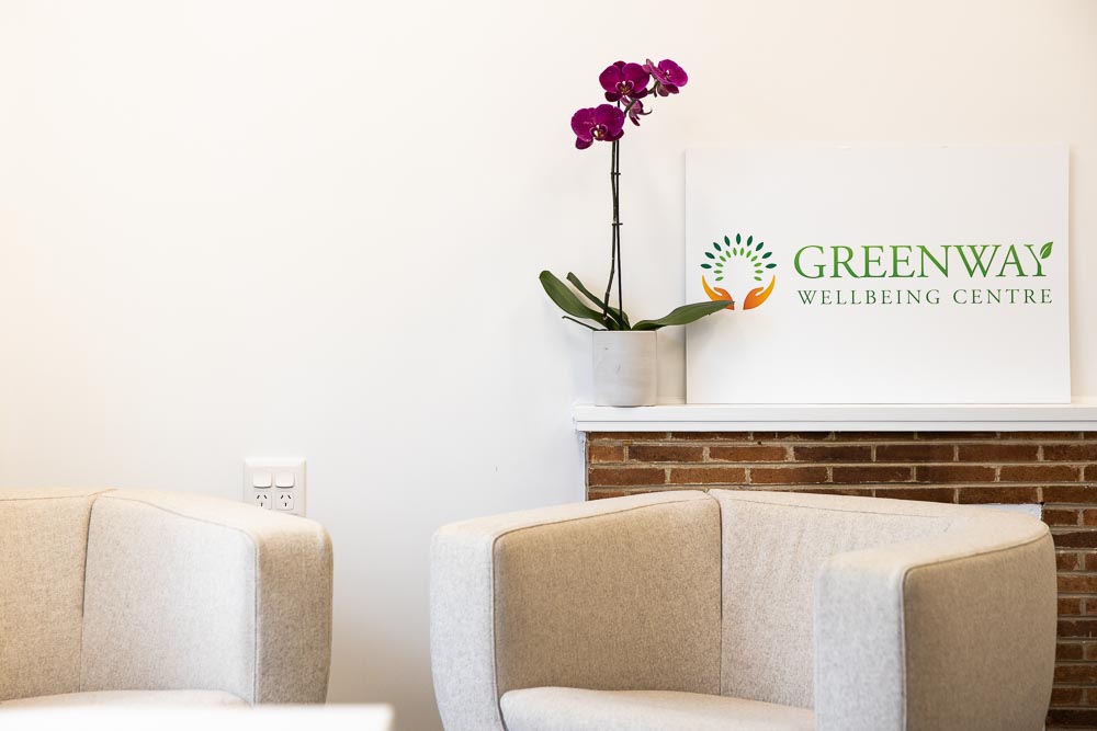 Two comfy chairs and a pot plant in front of a sign saying 'Greenway Wellbeing Centre'