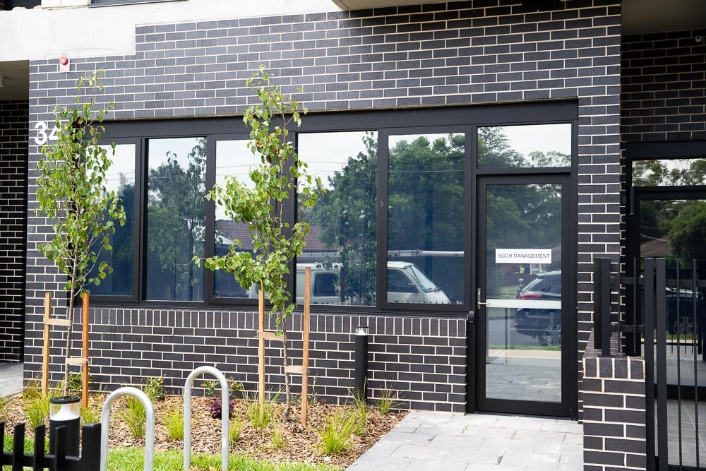 Ground floor office with reflective windows and dark brick and small garden. Sign on door reads SGCH Management
