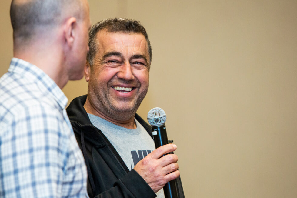 Two men talking, one is holding a microphone and laughing