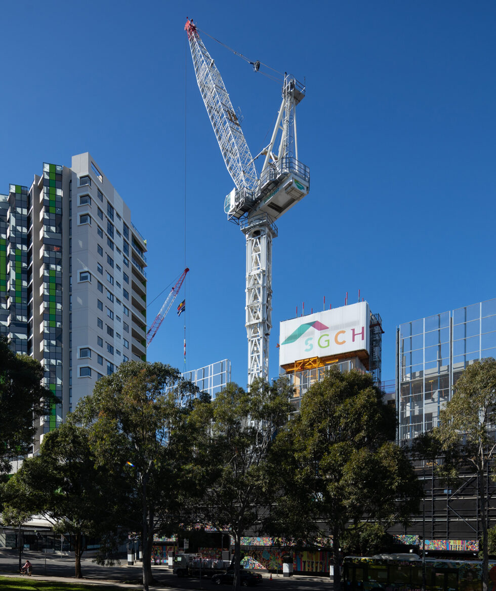 A high rise crane on a building site with scaffolding and large SGCH banner