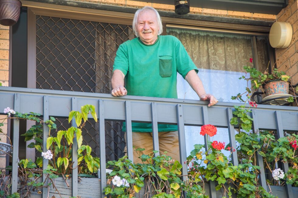 A smiling senior man looking down from his balcony with lots of pot plants