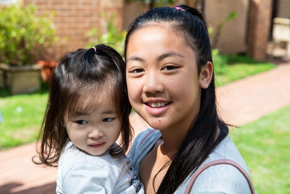 A smiling teenage girl holding a toddler outdoors