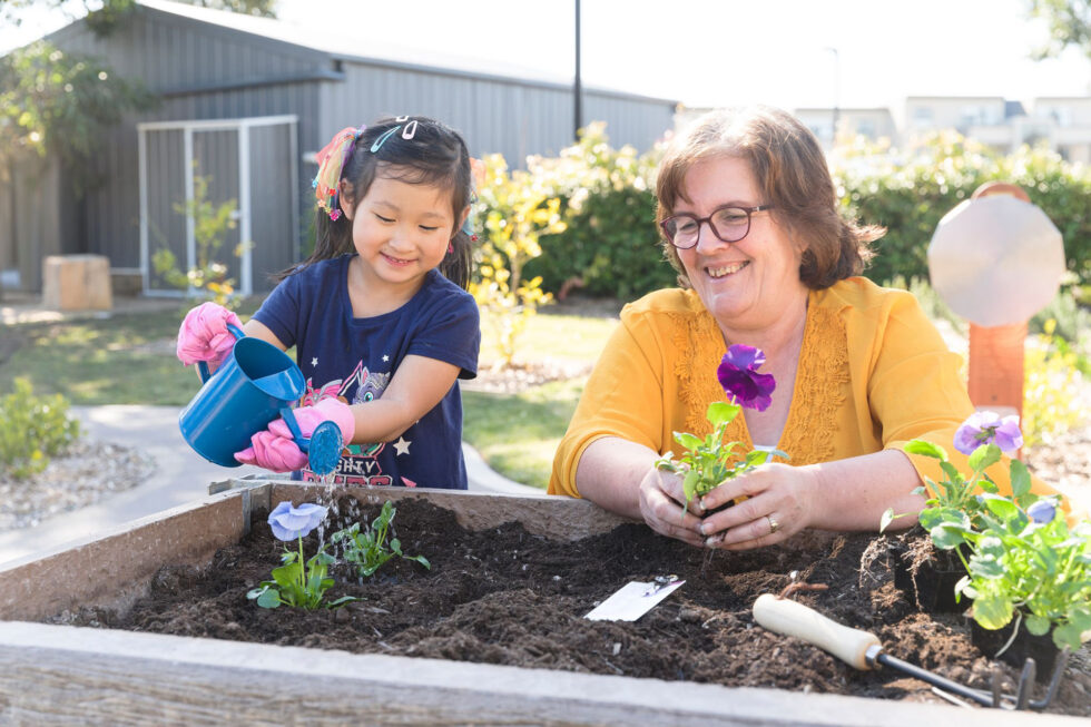 A young girl and older woman watering flowers in a planter box