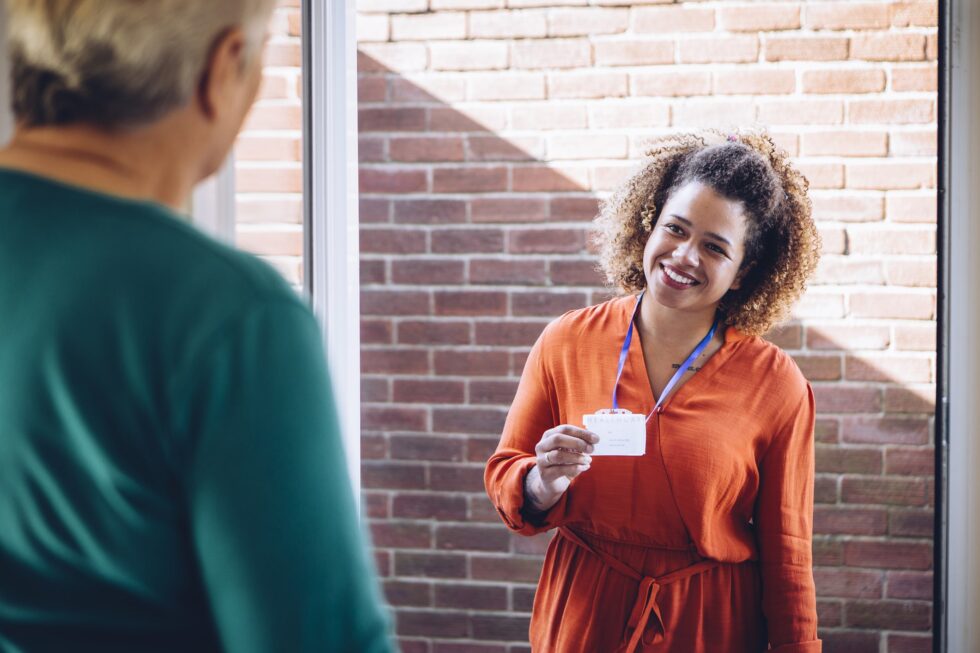 A staff member visiting someone at home showing their ID card at the door