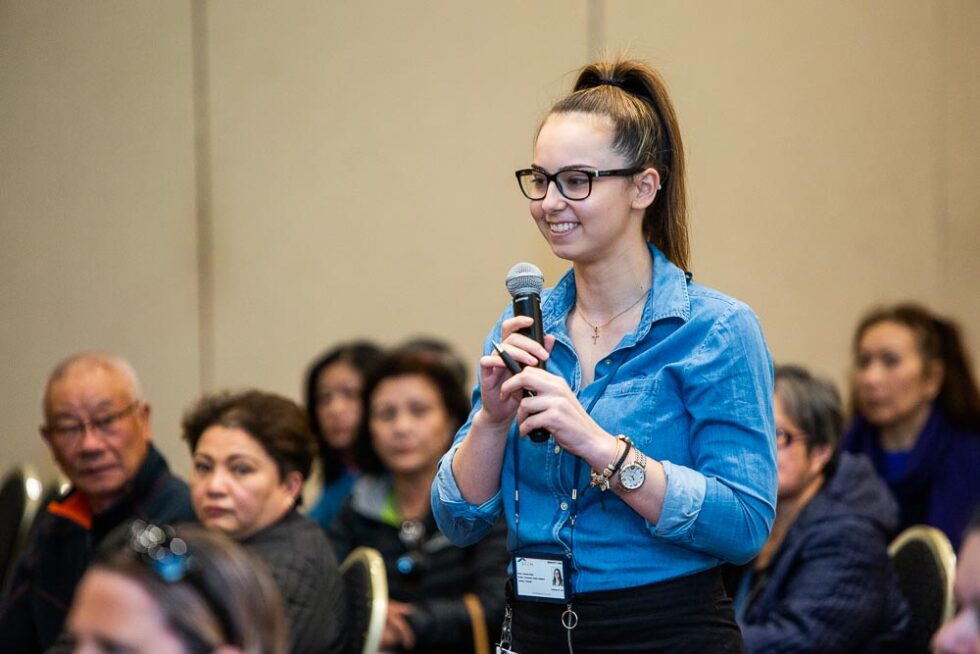 A young woman standing up in audience at a conference holding the microphone