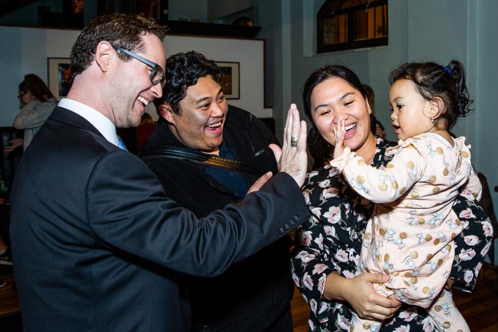 CEO Scott Langford high-fiving a toddler being held by her mum with smiling family nearby