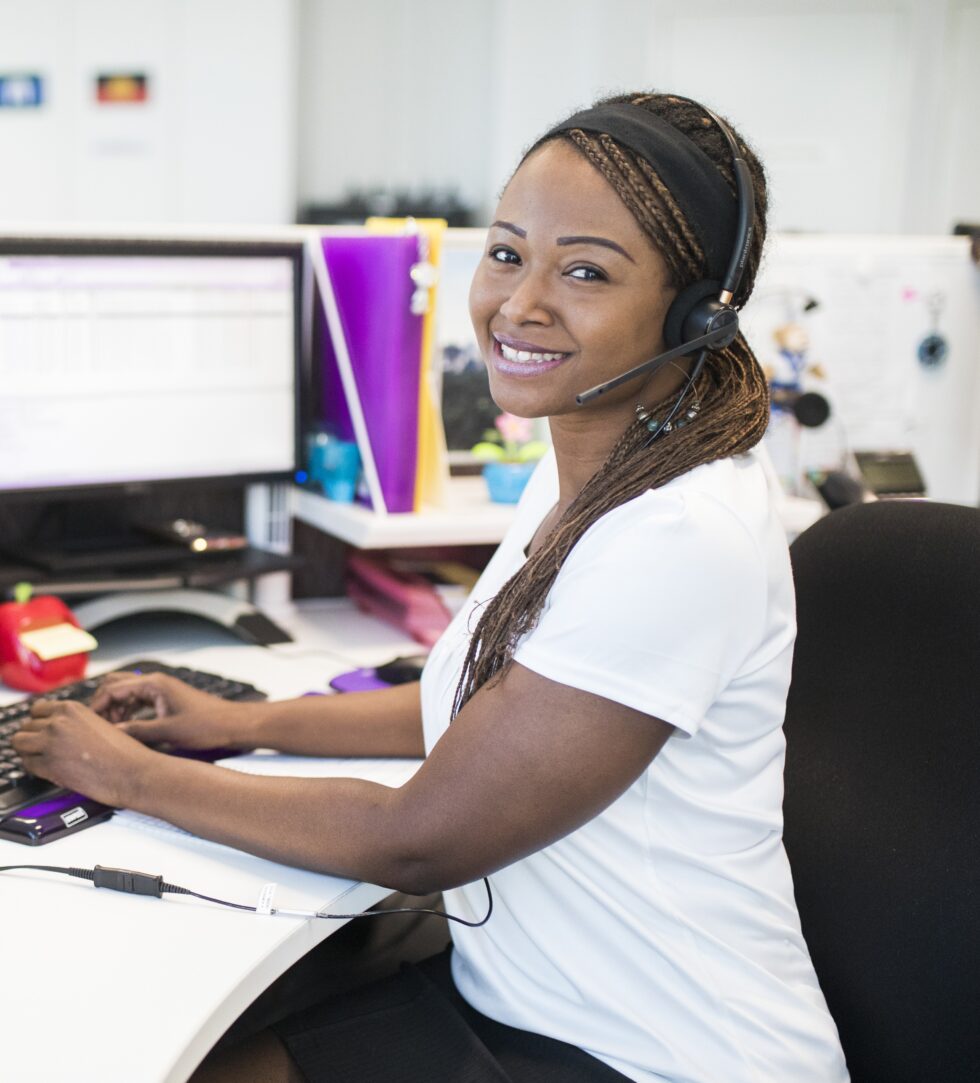 Smiling staff member sitting at her work desk wearing a phone headset