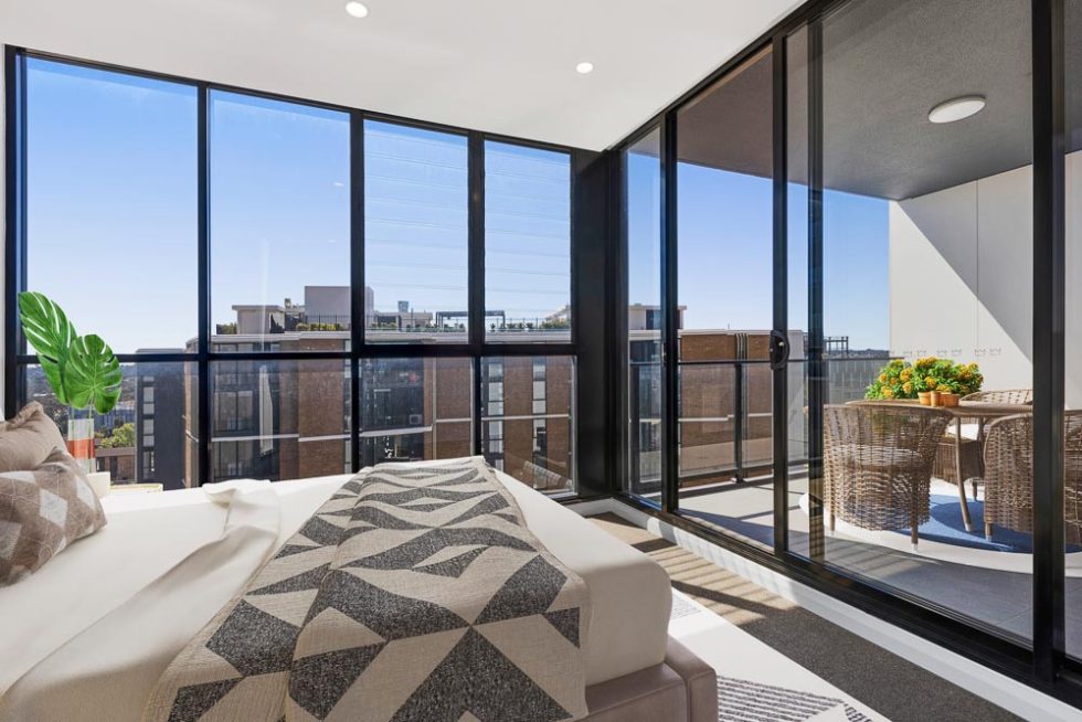 A bedroom with floor to ceiling windows and a view out over the suburbs