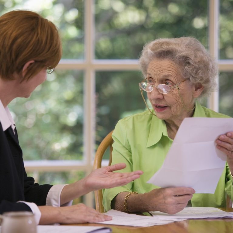 Senior woman discussing paperwork with younger woman at a table