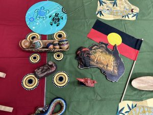 Various Indigenous artwork displayed on a table including painted eggs, wood cuts, table cloths and more