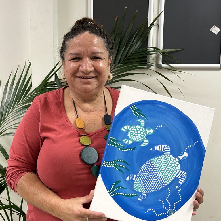 Maureen Clayton smiling and holding up Indigenous artwork of turtles