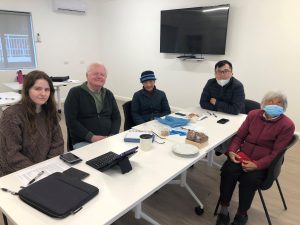Five smiling adults sitting around a table with their tech devices