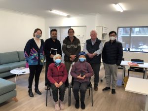 Seven smiling adults, some wearing masks, post for a photo indoors