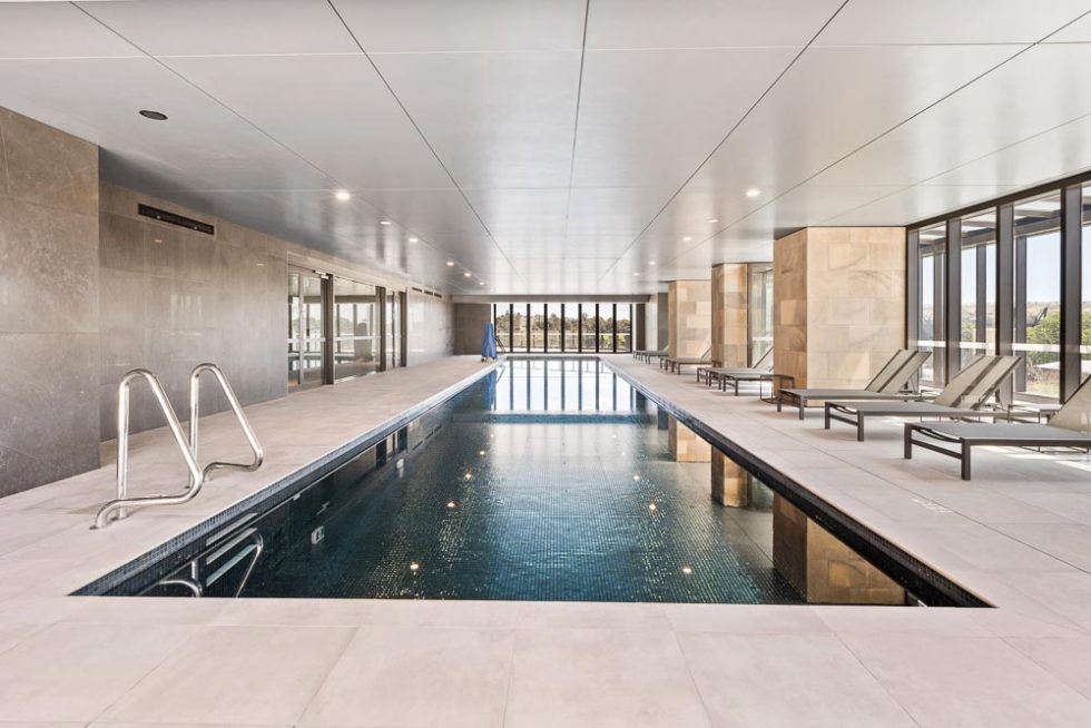 Modern indoor pool with wall-size windows looking out onto Parramatta and pool chairs along one side