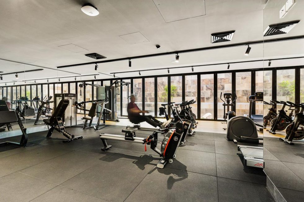 A gym area with well spaced workout machines and view out a wall of glass onto the street