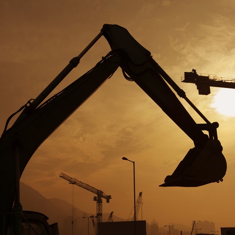 A silhouette of an excavator on a construction site at sunset