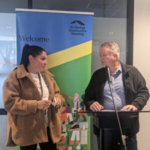 Partnerships Manager Bruce interviewing Aboriginal Housing Engagement Coordinator, Melissa, in front of a pull up banner that says Welcome